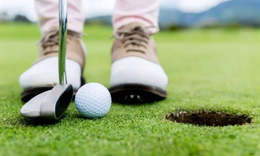 Golf player with spiked golf shoes hitting golf into hole.