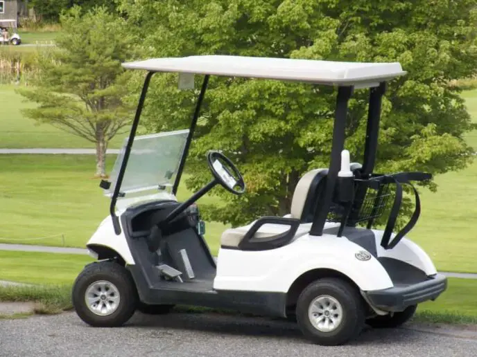 Golf cart stands outside on a sunny day.