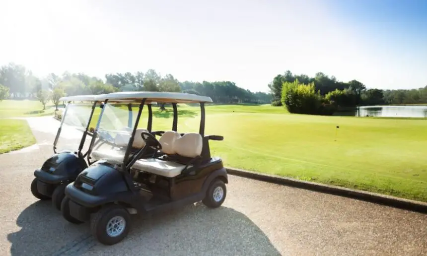 Two electrical golf carts standing at the parking lot of a golf club.